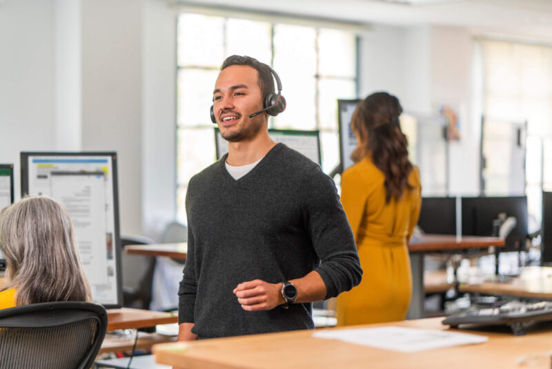 man standing in busy call centre talking to client with headset from desk phone