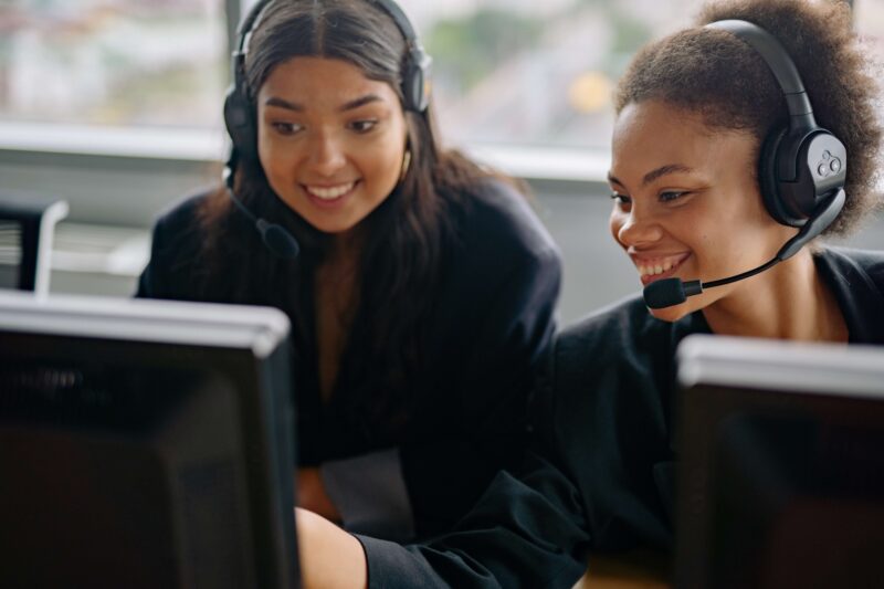 Image of two women wearing headsets and smiling looking at computer