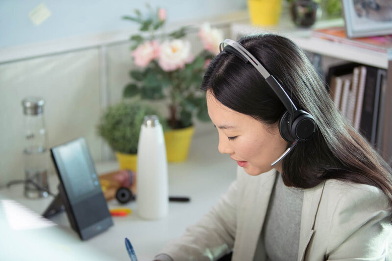 Image of woman wearing a Wireless Office headset writing a note with a pen