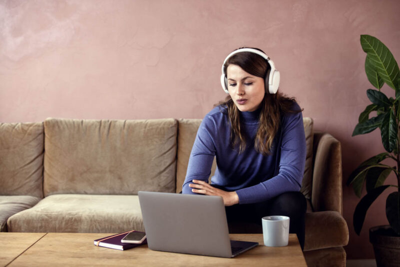 Woman wearing headset working on laptop on couch at home