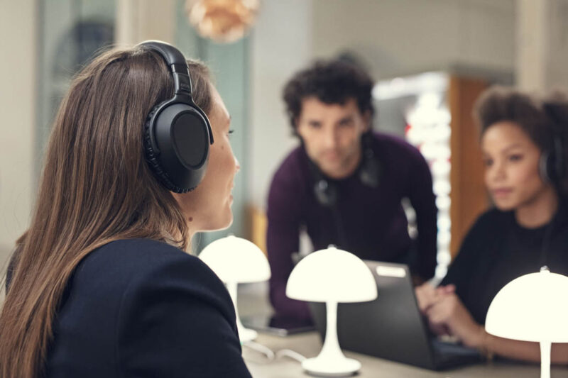 Woman wearing open ear headset leans into conversation in huddle room