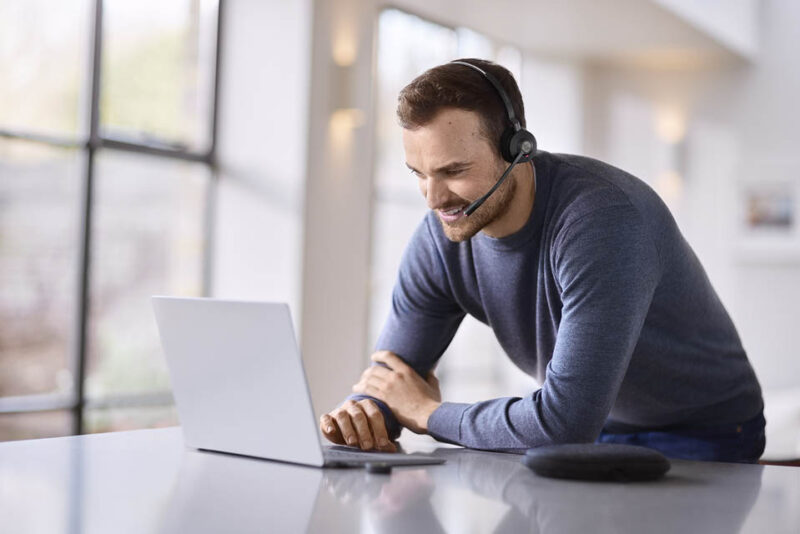 Man leaning into laptop smiling while wearing wireless headset 