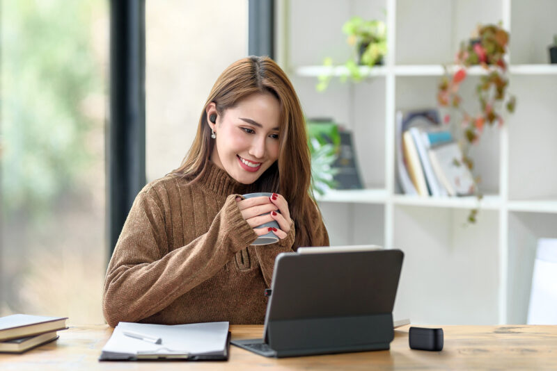 Woman wearing Jabra buds while drinking coffee and smiling on work call