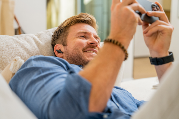 Man lying down on couch looking at phone wearing earphones